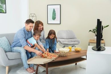 Family eating pizza while watching TV in room