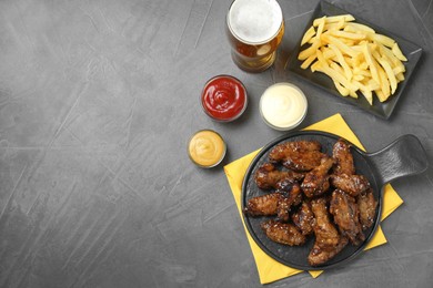 Tasty roasted chicken wings, sauces, french fries and glass of beer on black table, flat lay. Space for text