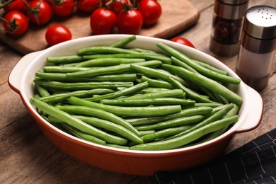 Raw green beans in baking dish on wooden table