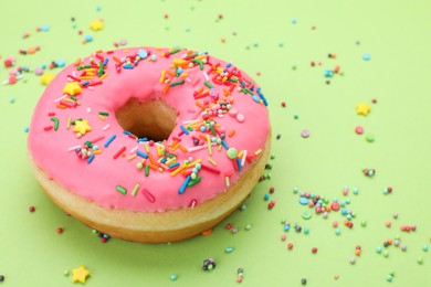 Photo of Glazed donut decorated with sprinkles on green background, closeup. Space for text. Tasty confectionery