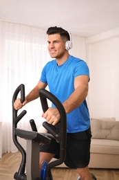 Man with headphones using modern elliptical machine at home