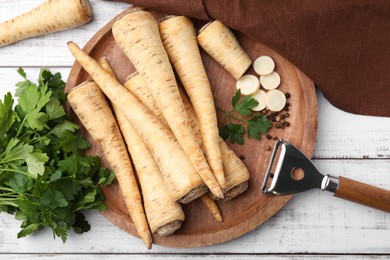 Photo of Raw parsley roots and bunch of fresh herb on white wooden table, flat lay