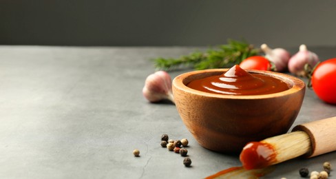 Photo of Tasty barbeque sauce in bowl, brush and peppercorns on grey textured table, closeup. Space for text