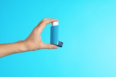 Photo of Female doctor holding asthma inhaler on color background, closeup view with space for text. Medical object