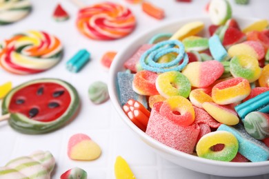 Bowl of tasty colorful jelly candies on white tiled table, closeup. Space for text