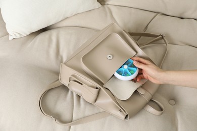 Woman putting pill box into backpack on sofa, closeup