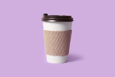 Photo of Takeaway paper coffee cup with cardboard sleeve on violet background