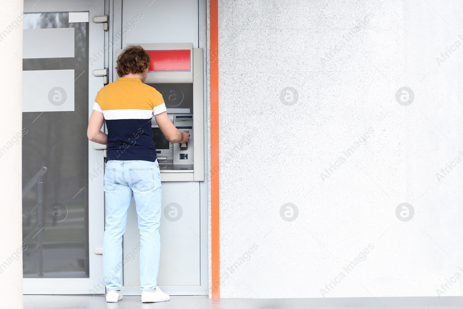 Photo of Young man using cash machine outdoors. Space for text