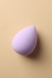 One violet makeup sponge on beige background, top view