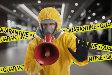 Image of Man wearing chemical protective suit with megaphone indoors. Prevention of virus spread
