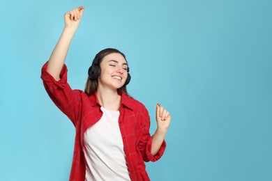 Happy woman in headphones enjoying music and dancing on light blue background, space for text