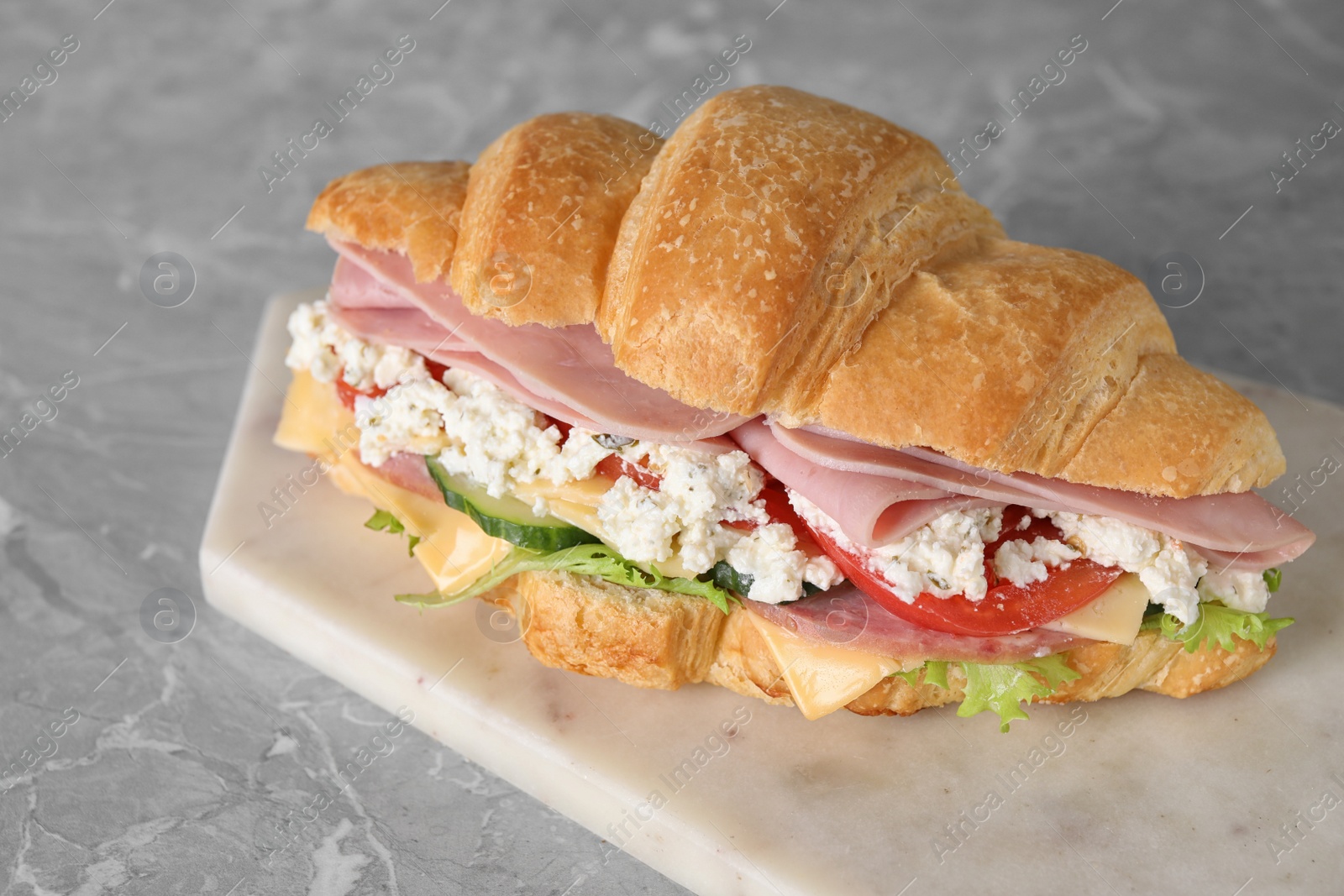 Photo of Tasty croissant sandwich with ham on grey marble table