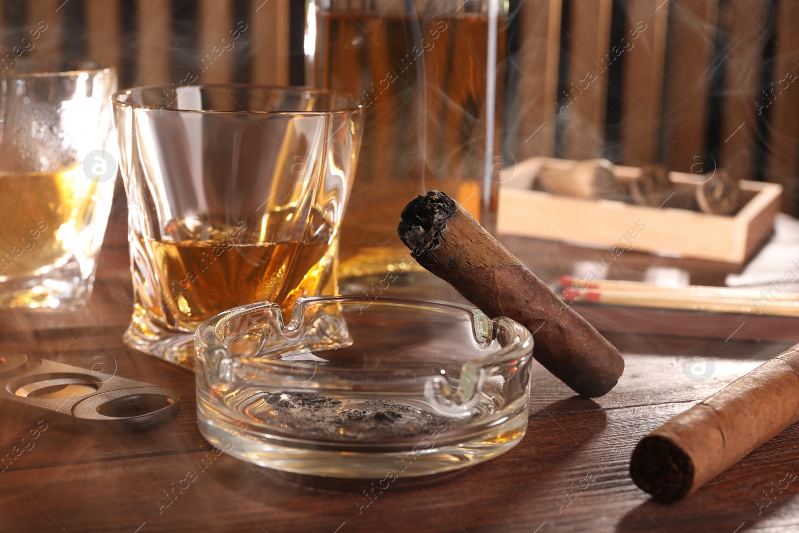 Photo of Cigars, ashtray, whiskey and cutter on wooden table, closeup