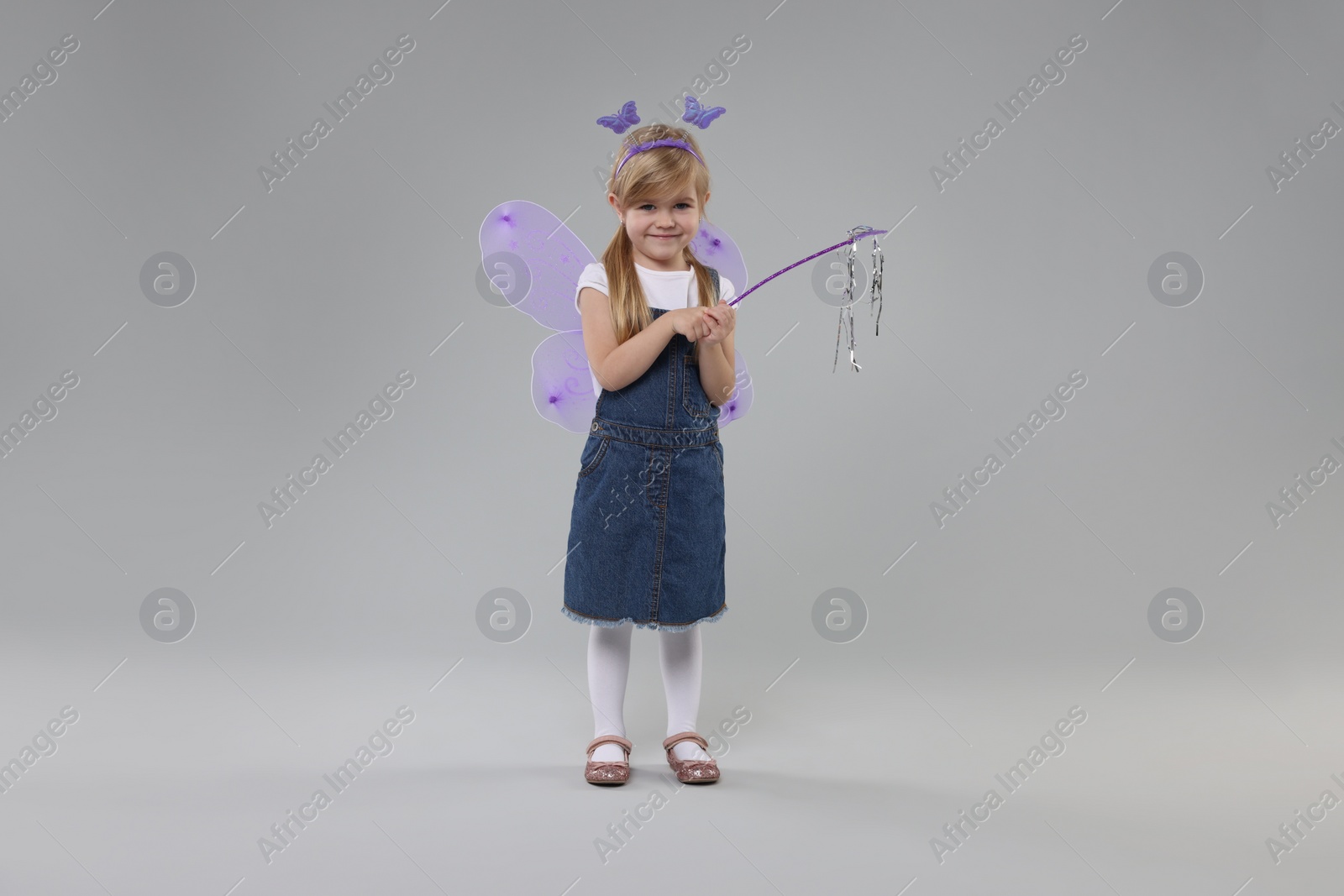 Photo of Cute little girl in fairy costume with violet wings and magic wand on light grey background