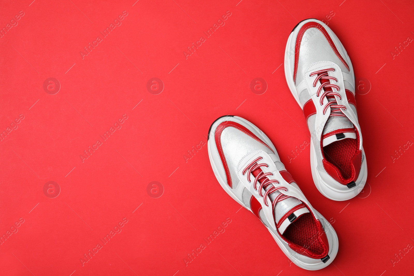 Photo of Stylish sneakers on red background, flat lay. Space for text