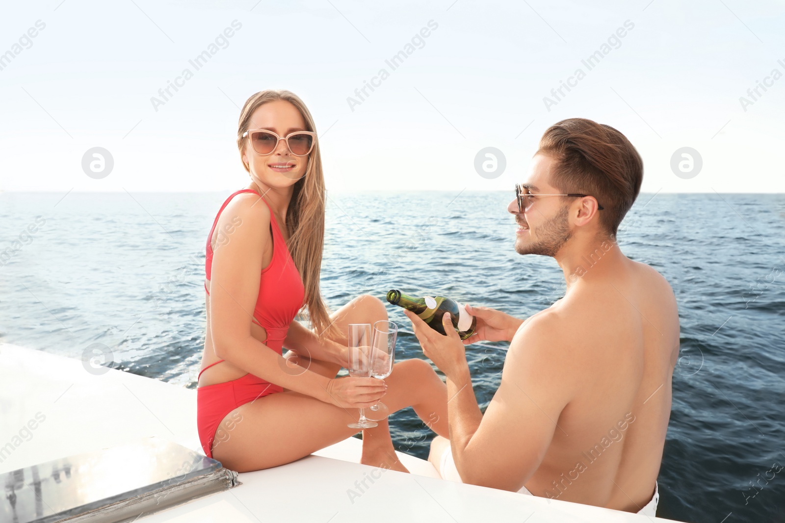 Photo of Young man and his girlfriend in bikini drinking champagne on yacht. Happy couple on vacation
