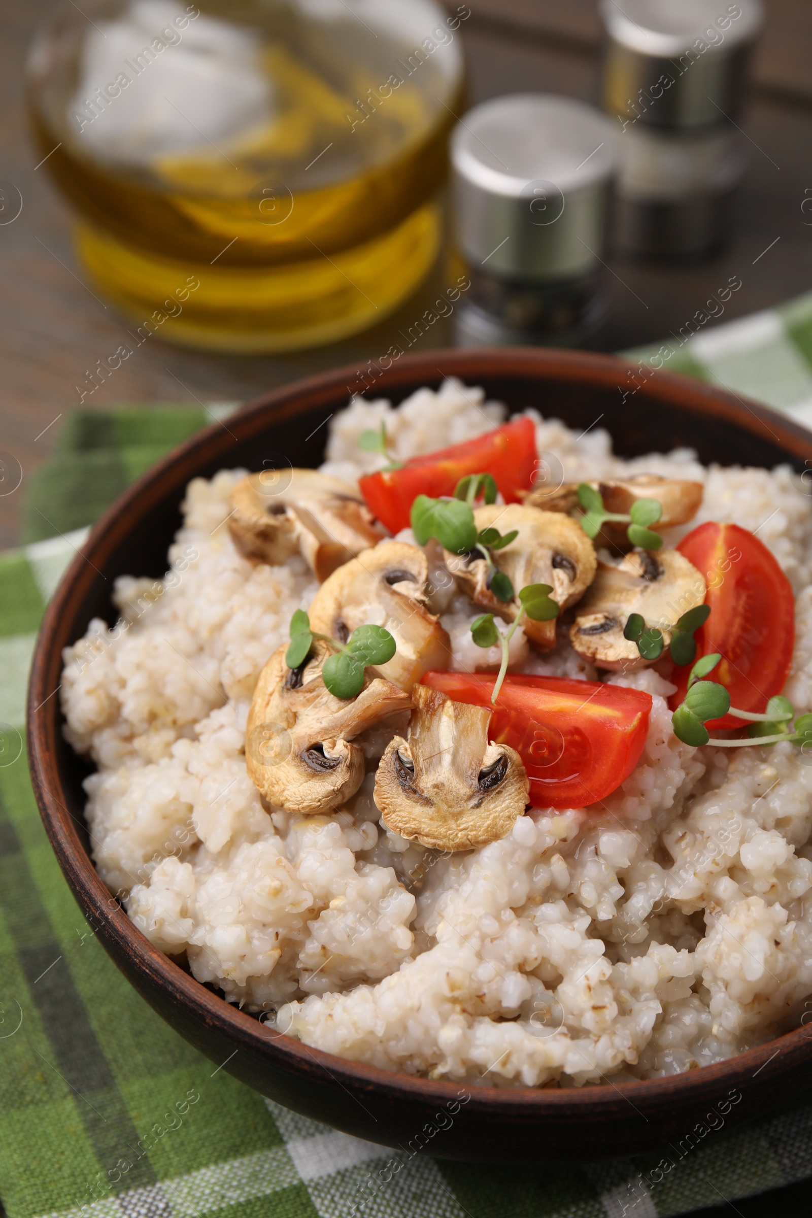 Photo of Delicious barley porridge with mushrooms, tomatoes and microgreens in bowl on table, closeup