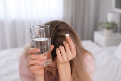 Photo of Upset young woman with abortion pill and glass of water at home