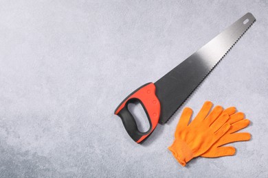 Saw with colorful handle and gloves on gray background, flat lay. Space for text