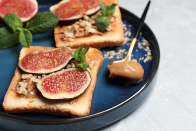 Photo of Tasty toasts served with fig, peanut butter and walnuts on white marble table, closeup