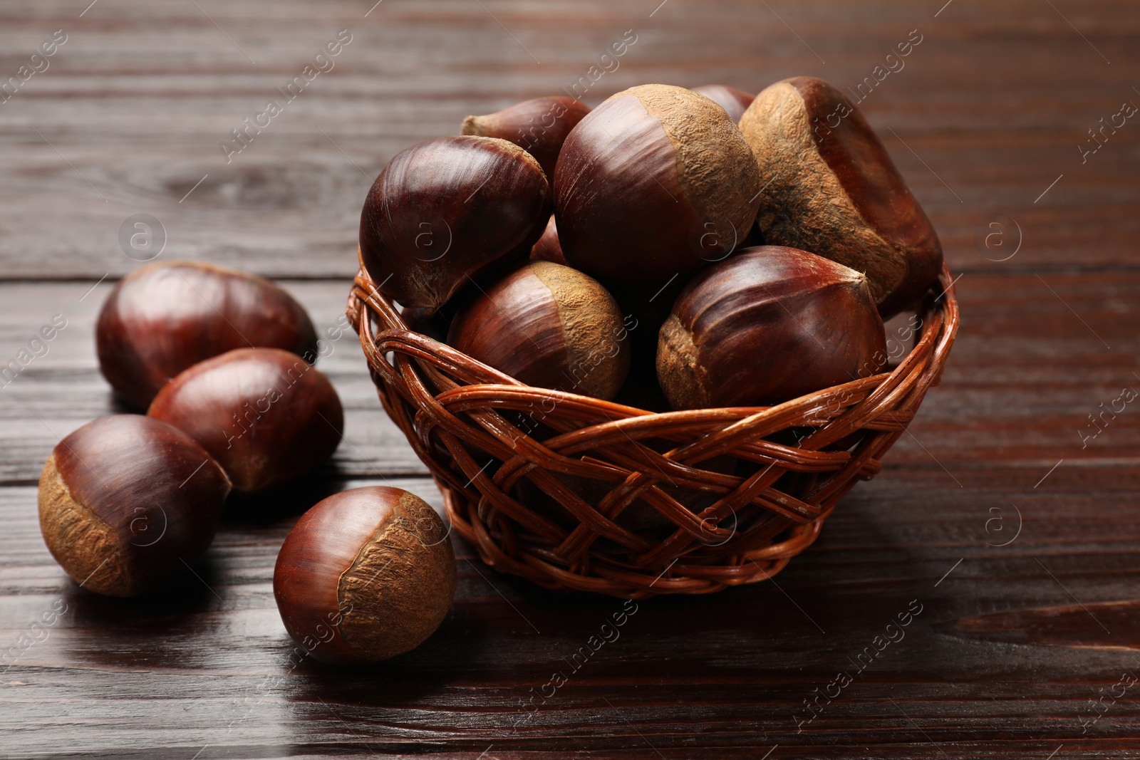 Photo of Sweet fresh edible chestnuts in wicker bowl on wooden table, closeup