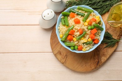 Delicious bulgur with vegetables in bowl, spices and oil on wooden table, top view. Space for text