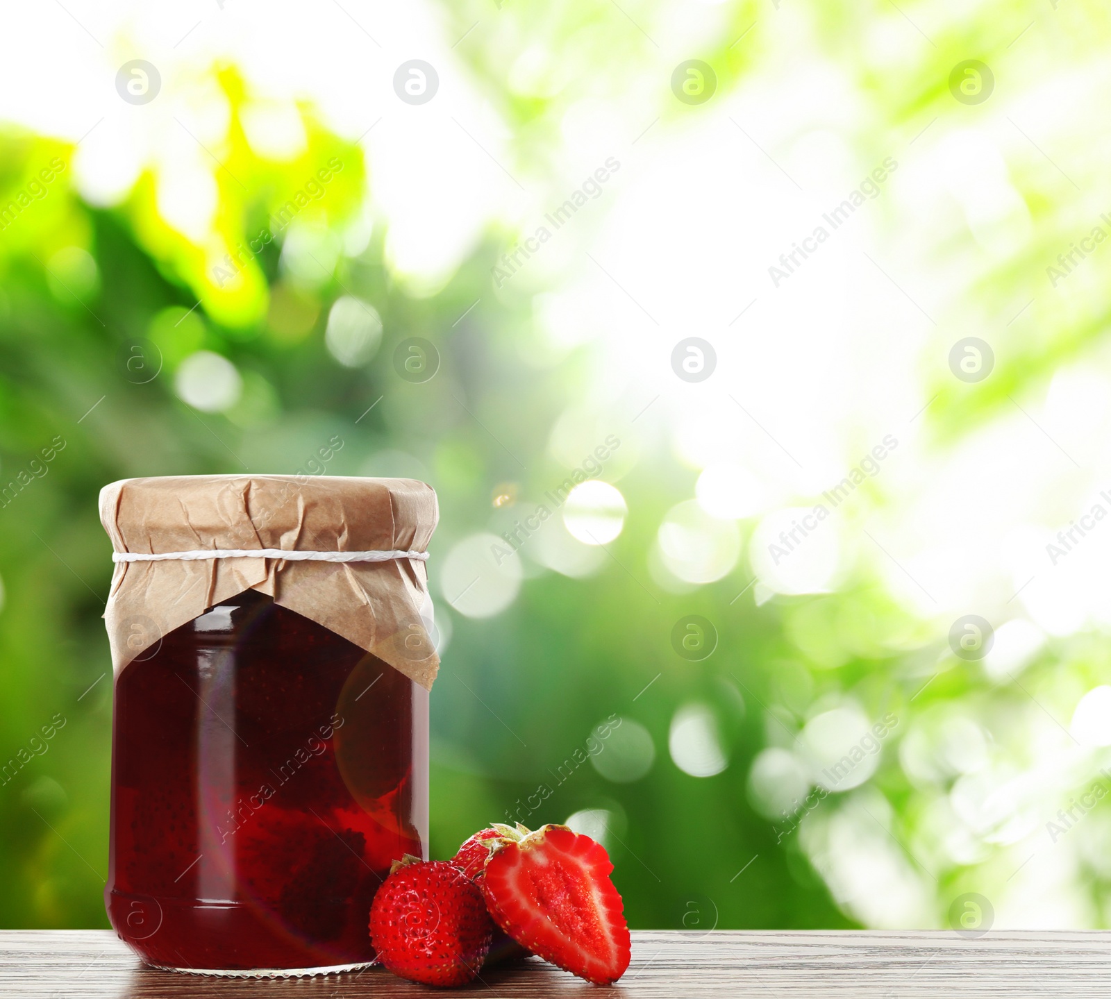 Image of Jar of tasty pickled strawberries on wooden table against blurred green background. Space for text