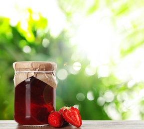 Image of Jar of tasty pickled strawberries on wooden table against blurred green background. Space for text