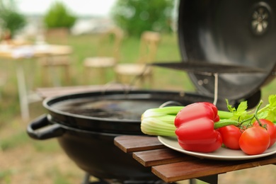 Photo of Plate with vegetables near barbecue grill outdoors, closeup