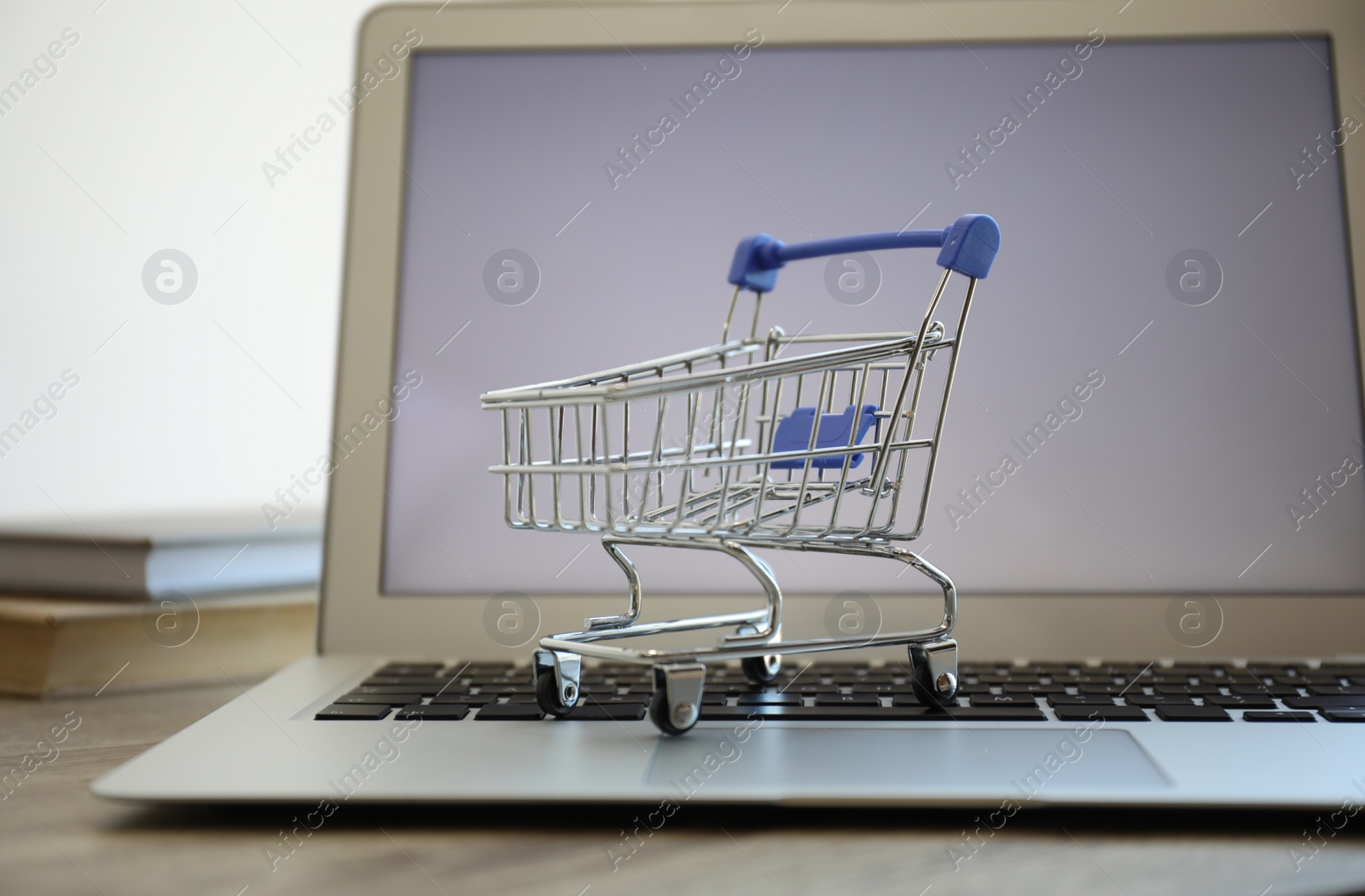 Photo of Internet shopping. Laptop with small cart on table, closeup