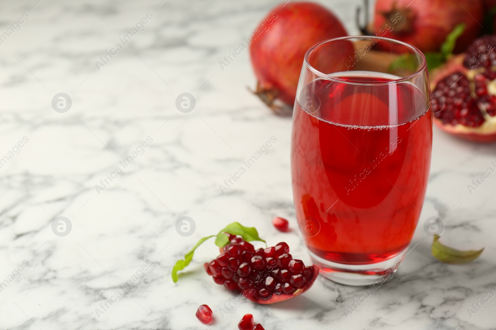 Photo of Tasty pomegranate juice in glass and fresh fruits on white marble table. Space for text