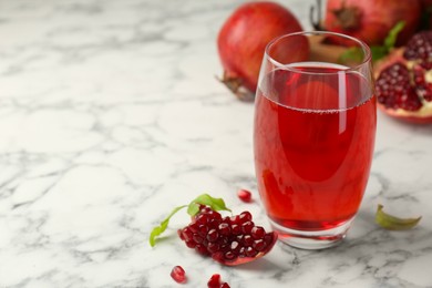 Photo of Tasty pomegranate juice in glass and fresh fruits on white marble table. Space for text