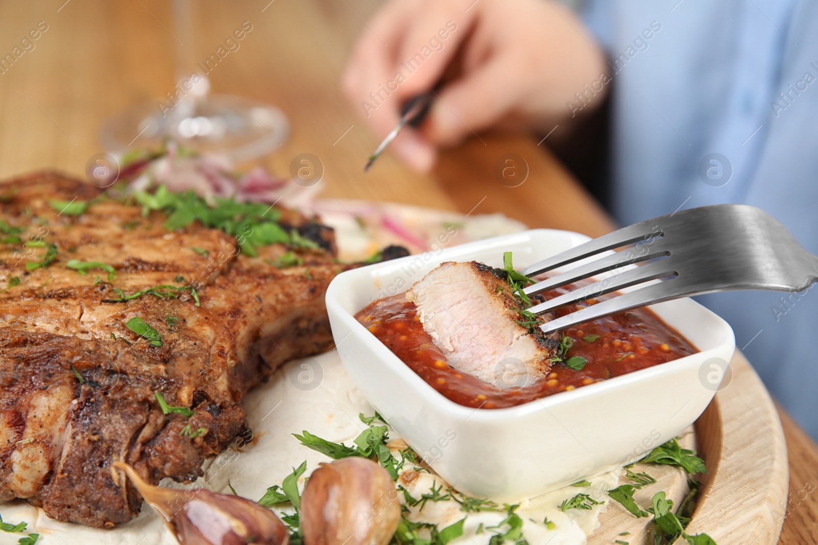 Photo of Woman eating delicious grilled pork chop at wooden table, closeup