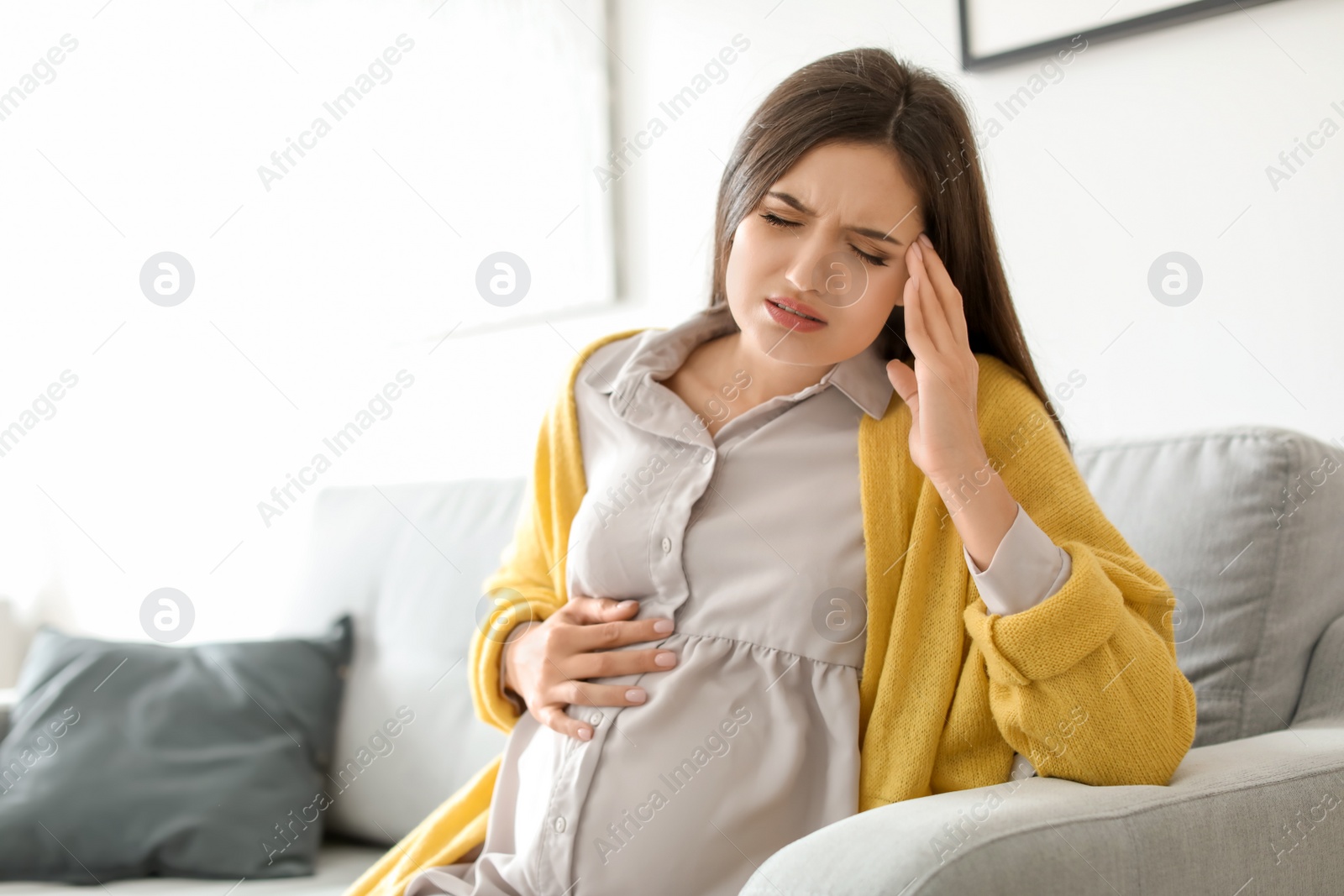 Photo of Young pregnant woman suffering from headache at home