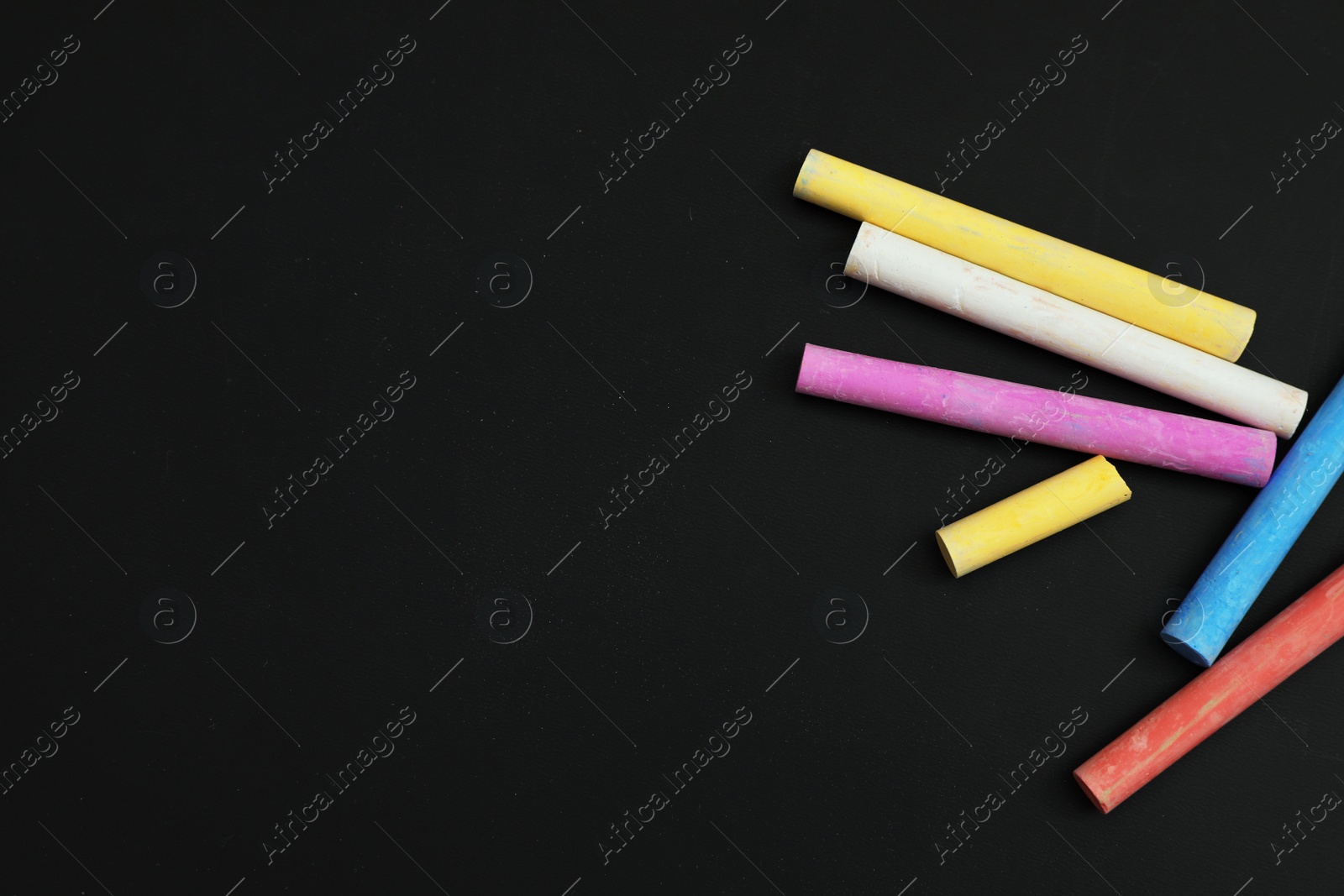 Photo of Colorful chalks on black board, flat lay. Space for text
