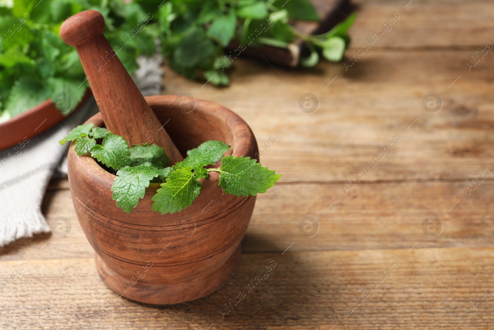 Photo of Mortar with pestle and fresh lemon balm on wooden table, space for text