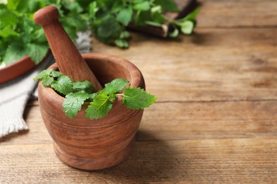 Photo of Mortar with pestle and fresh lemon balm on wooden table, space for text