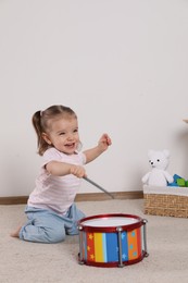 Cute little girl playing with drum and drumsticks at home