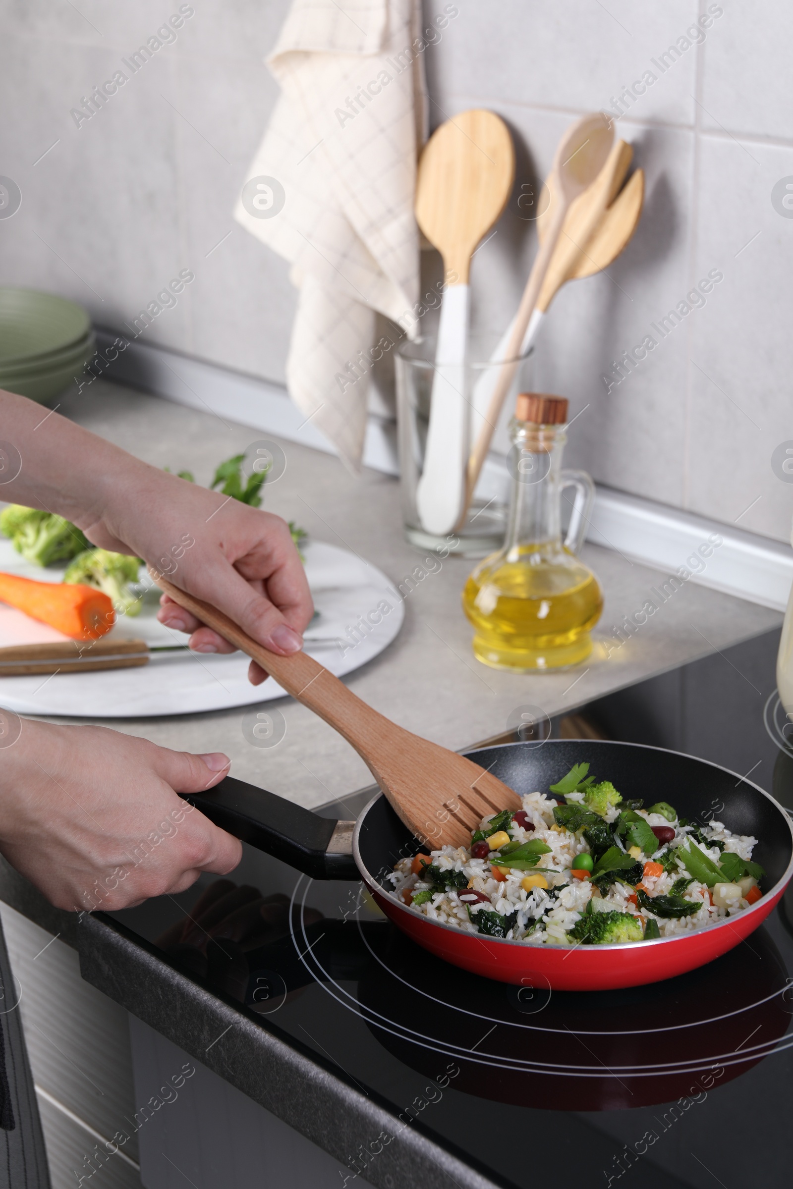 Photo of Woman frying rice with vegetables at induction stove in kitchen, closeup