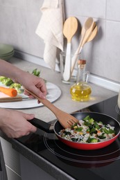 Photo of Woman frying rice with vegetables at induction stove in kitchen, closeup