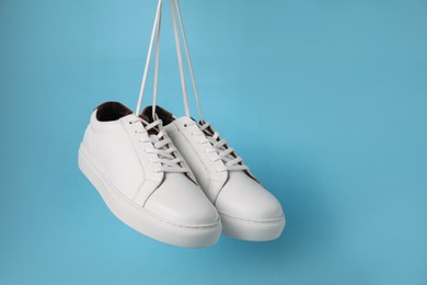 Photo of Pair of stylish white sneakers hanging on light blue background, space for text