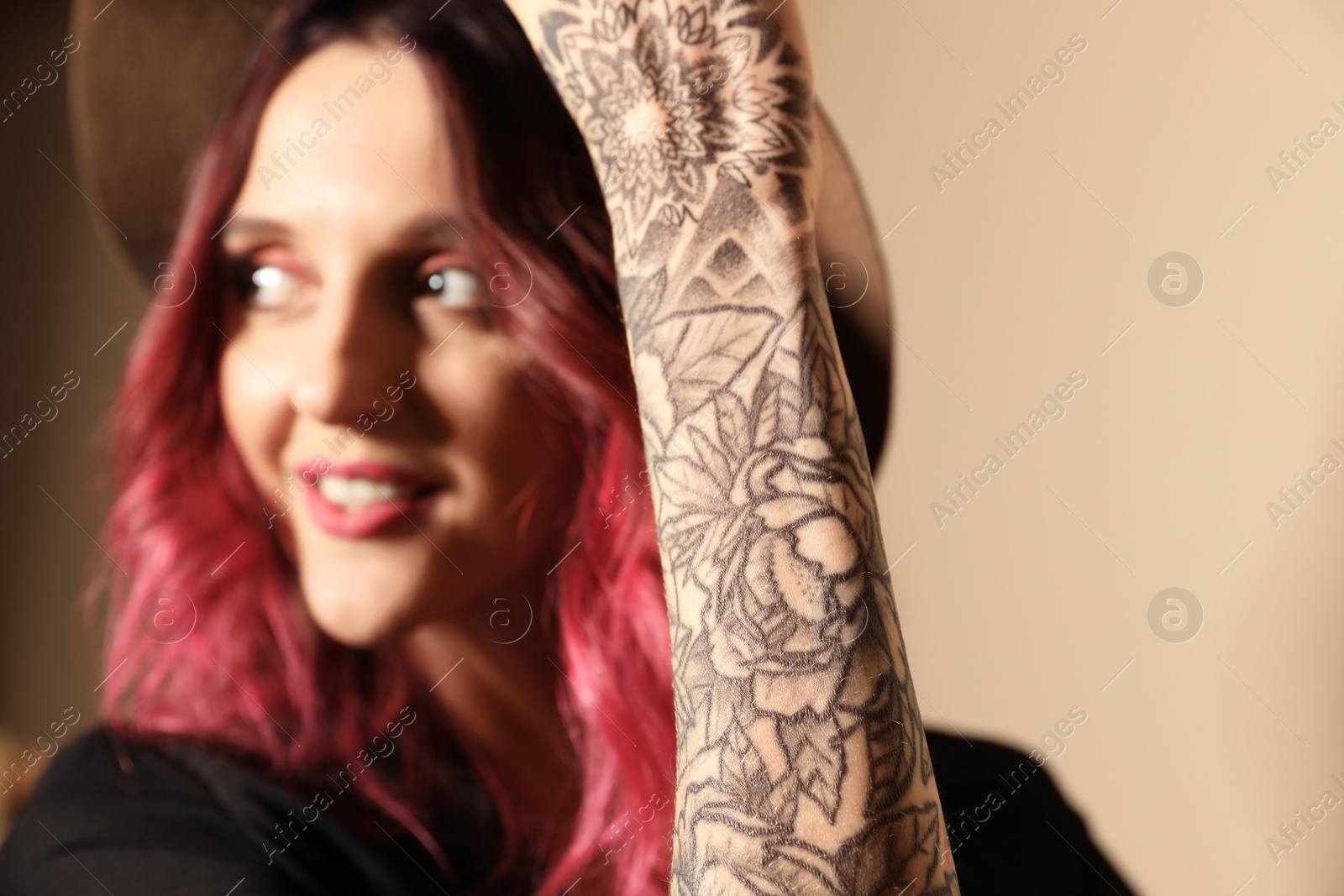 Photo of Beautiful woman with tattoos on arm against beige background, focus on hand