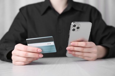 Photo of Online payment. Woman with smartphone and credit card at white wooden table, closeup