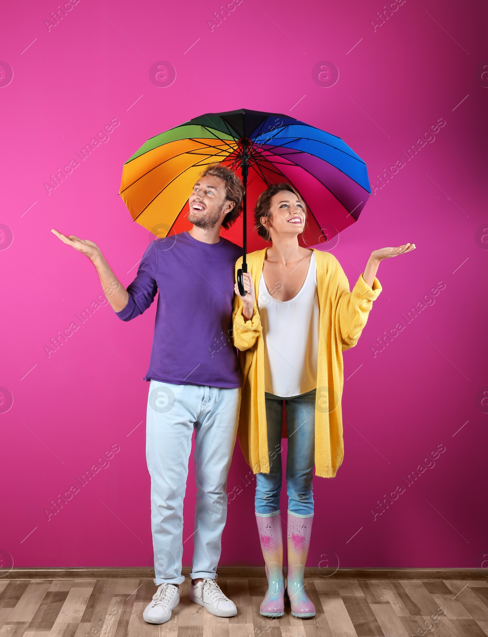 Photo of Couple with rainbow umbrella near color wall