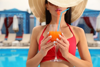 Young woman in stylish red bikini with cocktail near swimming pool
