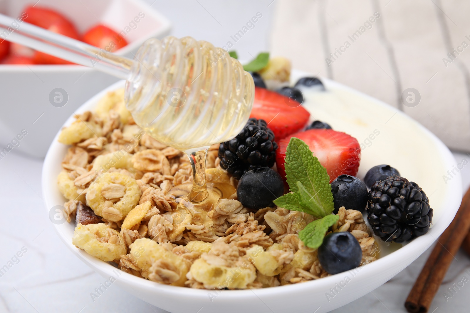 Photo of Pouring honey onto tasty oatmeal and fresh berries in bowl, closeup. Healthy breakfast