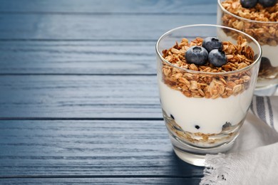 Photo of Glasses of tasty yogurt with muesli and blueberries on blue wooden table. Space for text
