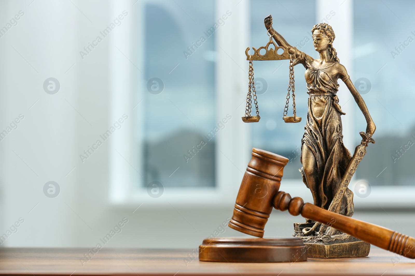 Photo of Figure of Lady Justice and gavel on wooden table indoors, space for text. Symbol of fair treatment under law