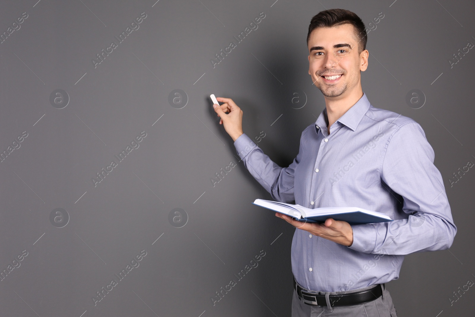 Photo of Young male teacher with book and chalk on grey background