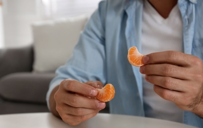 Man with tangerine slices at table indoors, closeup